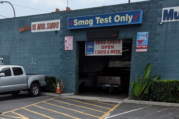 Exterior of a smog check station with signs for "15 min. smog," "Smog Test Only," and "Smog Check Open 7 Days a Week.