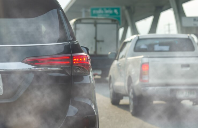 Cars in traffic emit exhaust fumes, creating visible air pollution on a city road near an overpass, highlighting the need for regular local smog check services.
