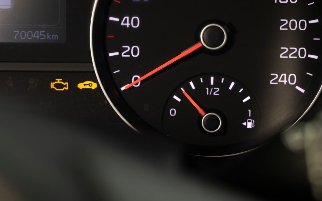 Close-up of a car dashboard showing warning lights and speedometer at zero with a low fuel gauge.